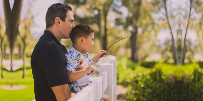 A man holds his son at a fence after learning more about how to sign up for clinical studies and the potential benefits of a study.